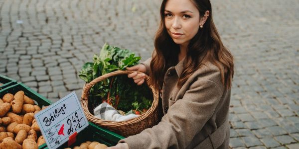Young woman shopping at Erfurt farmers market, holding basket with fresh vegetables. Capturing local shopping culture.