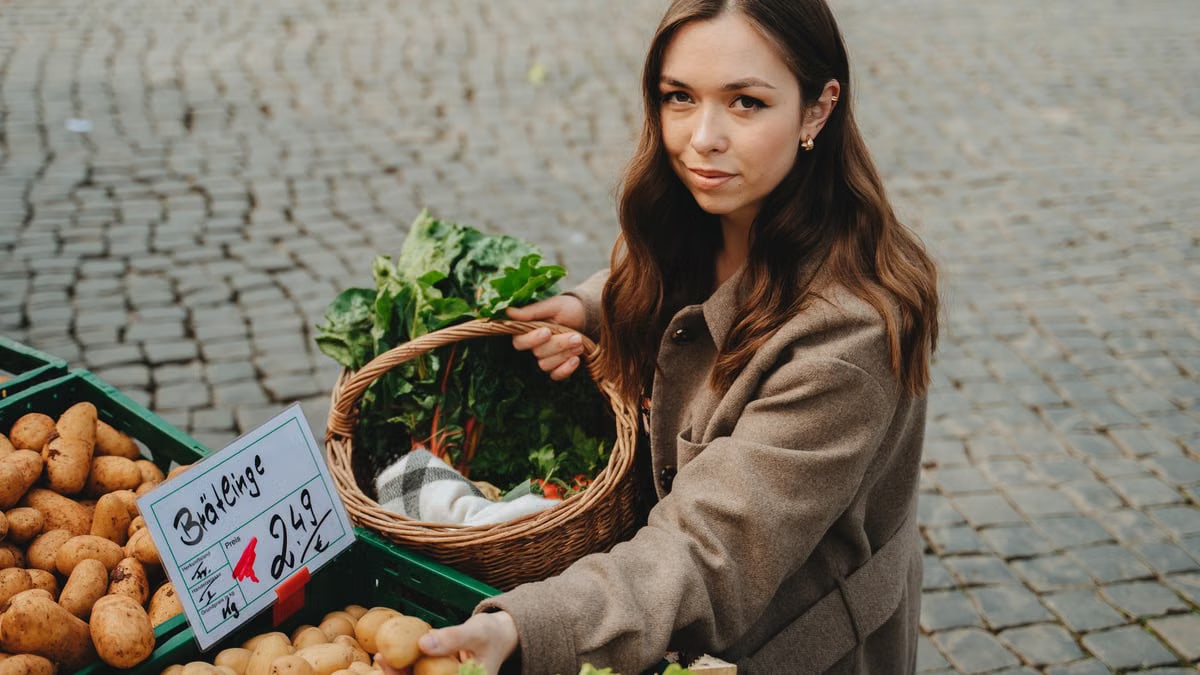 Young woman shopping at Erfurt farmers market, holding basket with fresh vegetables. Capturing local shopping culture.