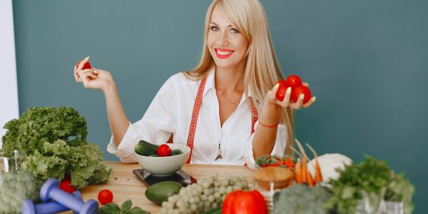 Healthy lifestyle concept with woman holding tomatoes and surrounded by fresh vegetables in a studio setting.